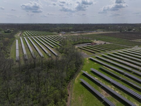 Aerial view of rows of solar panels reflecting the sky's light, contrasting with the green grass and trees, Lebanon, Ohio, United States.