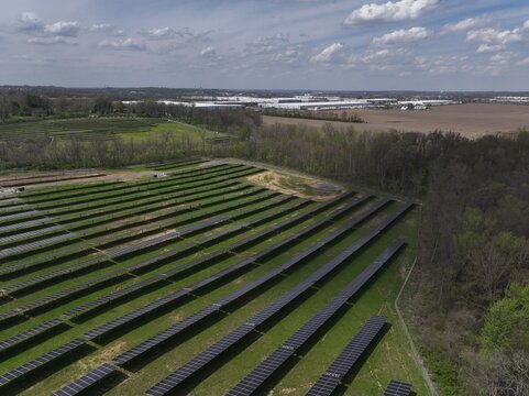 Aerial view of rows of solar panels glinting under the sun's glare near a sprawling industrial complex, Lebanon, Ohio, United States.