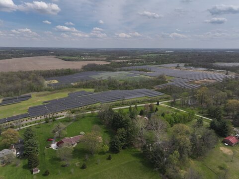 Aerial view of sprawling solar panels glinting under the diffused sunlight, contrasting with the surrounding fields and trees, Lebanon, Ohio, United States.