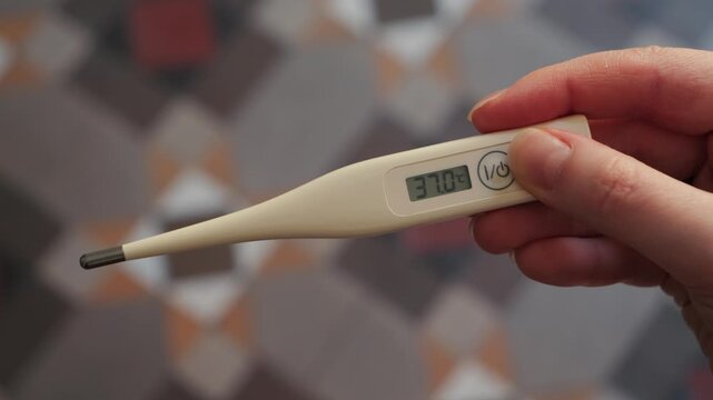 Close-up of hands holding a digital thermometer showing a temperature of 37 on the display. Concept of health monitoring and body temperature check. High quality 4k footage