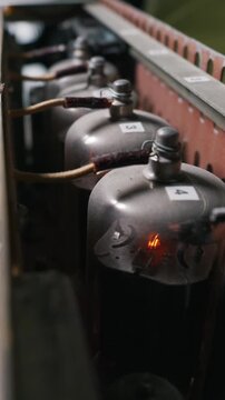 Vacuum tubes in a homemade audio amplifier glow brightly inside the metal chassis, connected by vintage cloth wires. This illustrates the concept of retro radio engineering technology.