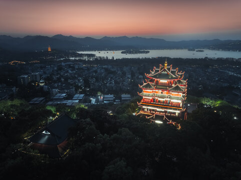 Aerial view of a majestic, multi-tiered pagoda glowing brilliantly in red and white on a dark hill overlooking the serene West Lake under a twilight sky, Hang Zhou Shi, Zhe Jiang Sheng, China.