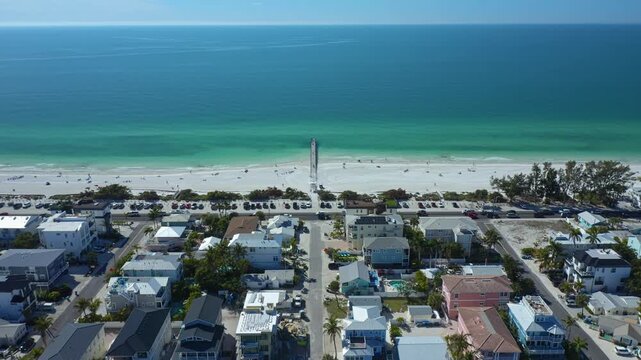 A pier stretches into the quiet sea, flanked by rows of beachfront homes and parked cars. Ideal for real estate or travel content.