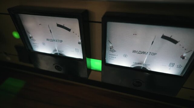 Vintage analog meters glow on a retro audio amplifier. The Russian word Indicator is printed on the dials measuring sound decibel levels. Bright green lights illuminate the equipment.