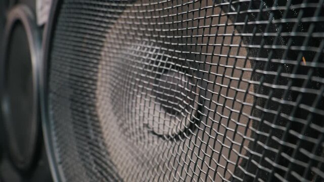 Detailed close up of a black metal protective mesh grill covering a professional audio speaker cone. Shallow depth of field highlights the rigid woven texture against the dark blurred background.