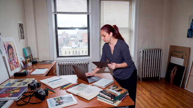 Attentive visual artist reviewing portfolio materials in urban apartment studio workspace