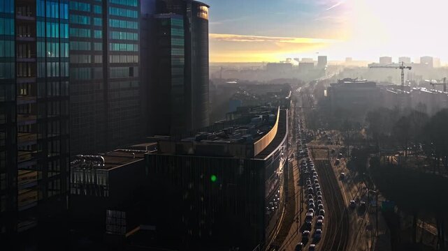 City skyline aerial view skyscrapers traffic street sunset lighting. Modern urban architecture glass buildings dense vehicle congestion road. Golden hour sunlight hazy horizon European metropolis