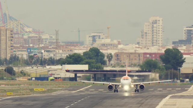 A commercial passenger jet, an Airbus A320, accelerates down the runway and takes off with a bustling city skyline and port cranes in the background. Heat haze shimmers from the engines,