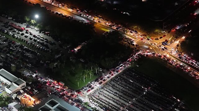 Aerial night view of vehicle light trails and parked cars at a busy intersection and parking area at Batu Kawan Stadium