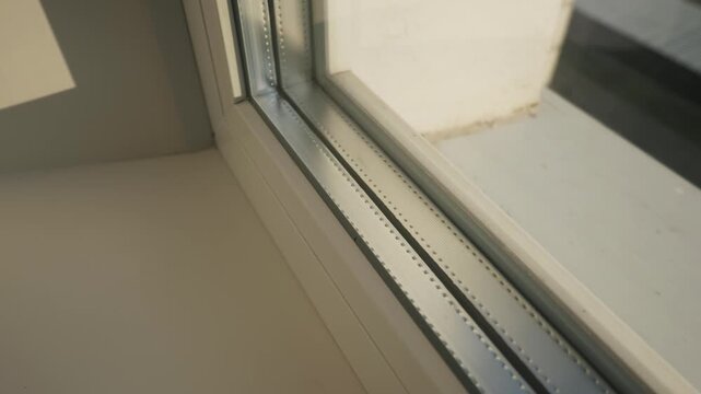 Triple pane window corner displays metal spacer bars and white frame in macro view highlighting insulation technology. Concept of energy efficiency and home thermal insulation performance.