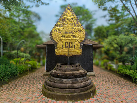 Javanese Gunungan Wayang Sculpture: Golden Tree of Life with intricate carvings on a stone pedestal, set against a lush traditional garden with a soft blurred background.