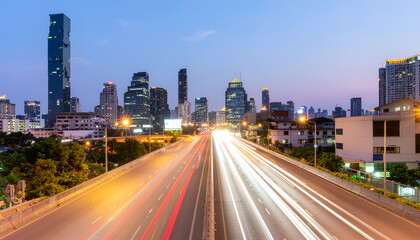 Fototapeta premium Modern city skyline with fast highway light trails at twilight.