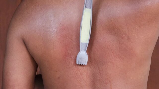An Asian man scratches his back to relieve an itch with a back scratcher.