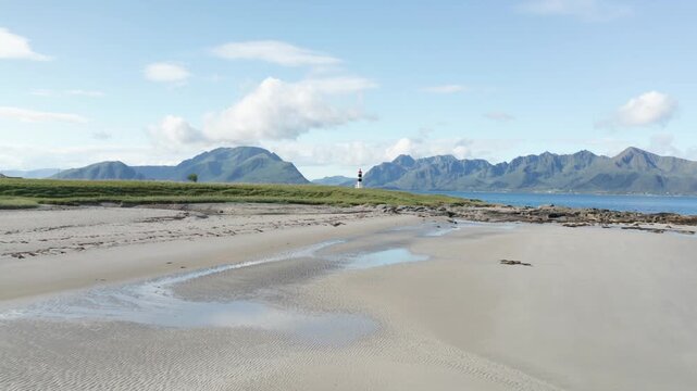 Dramatic aerial drone footage flying along a dark moody Norwegian mountain coastline with steep slopes plunging into the deep blue sea below under dramatic cloudy skies, panning ove lighthouse
