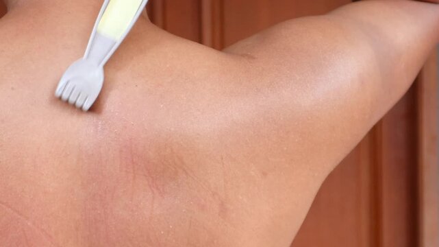 An Asian man scratches his back to relieve an itch with a back scratcher.