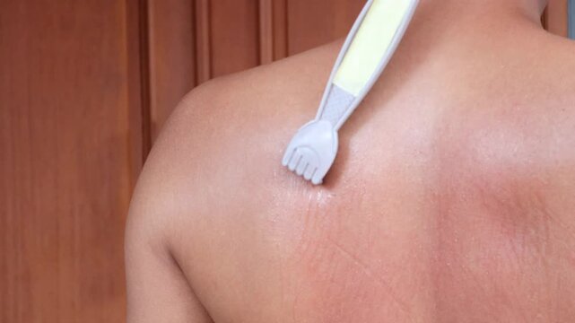 An Asian man scratches his back to relieve an itch with a back scratcher.