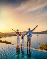 A happy family on summer holidays stands by the swimming pool and enjoys the beautiful sunset...