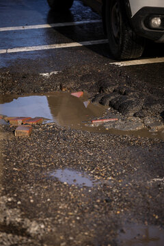 Urban scene with car passing by a big pothole in the asphalt