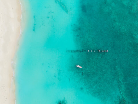 Aerial view of white sand beach meeting brilliant turquoise waters, a small boat near wooden pilings, Hoarafushi, Thiladhunmathee Uthuruburi, Maldives.
