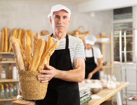 Elderly man with basket of baguettes in bakery