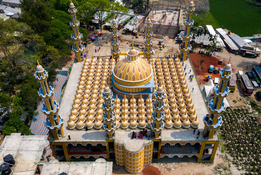 Aerial view of a majestic mosque with gleaming golden domes and towering minarets amidst verdant surroundings and ongoing construction, Tangail, Dhaka Division, Bangladesh.