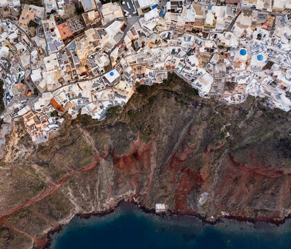 Aerial view of the iconic white-washed buildings cascading down the dramatic volcanic cliffs into the deep blue Aegean Sea, Fira, Thira, Greece.