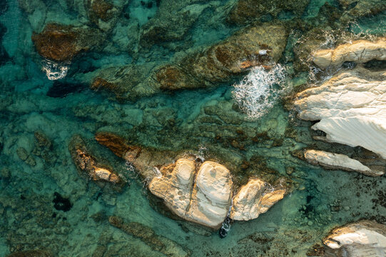 Aerial view of vibrant turquoise waters revealing ancient rock formations, contrasting dark and light tones with foamy white wave patterns, Thira, Thira, Greece.