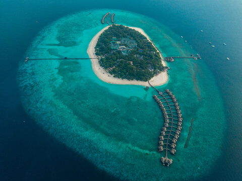 Aerial view of a lush, green island encircled by turquoise waters, connected by elegant overwater bungalows and walkways, Hoarafushi, Maldives.