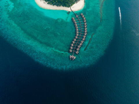 Aerial view of overwater bungalows on a bright turquoise reef, beside a white sand island and dark blue ocean, Hoarafushi, Thiladhunmathee Uthuruburi, Maldives.
