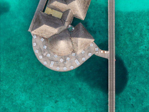 Aerial view of thatched roofs and sun-kissed decks meet the turquoise embrace of the ocean, connected by a sleek wooden walkway, Hoarafushi, Maldives.
