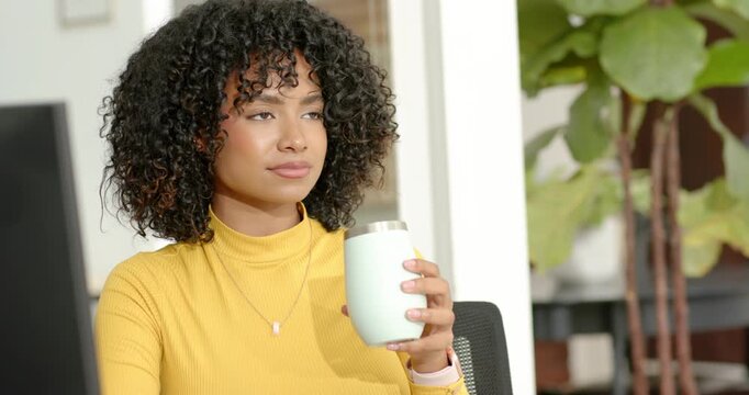 Woman in mustard turtleneck pausing, smelling and sipping seafoam tumbler to refocus at desk
