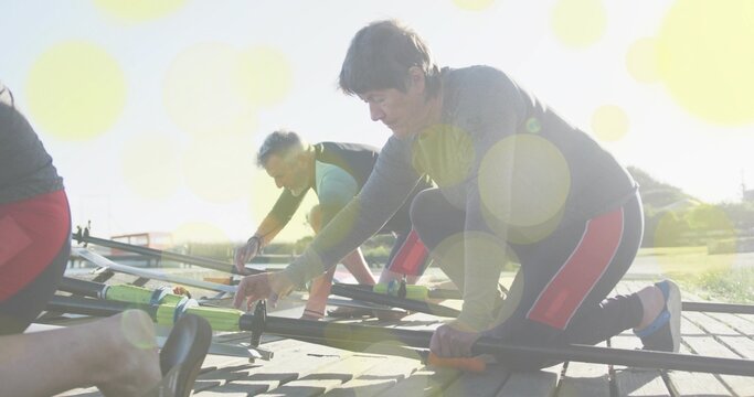 Kneeling mature female rower adjusting neon green oarlock on dock in bright sun, redpanel leggings