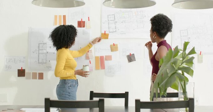 Diverse team left woman placing first note, gesturing and adjusting swatches on moodboard at studio