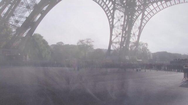 Visitors arriving crossing plaza under Eiffel Tower arch pausing at rails snapping pics for tourism
