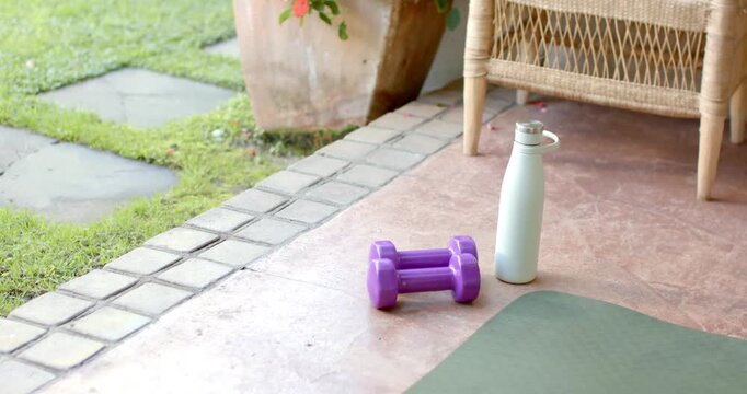 Camera is panning right on covered porch to reveal purple dumbbells and rotating water bottle