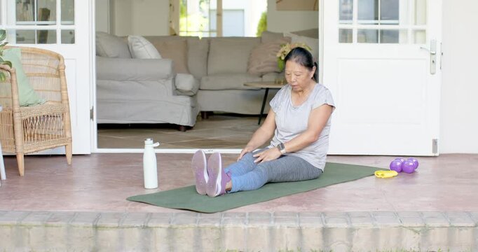 Asian senior female finishing hamstring stretches on porch then reaching band deepening stretch