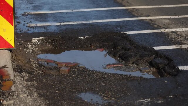 Urban scene with car passing by a big pothole in the asphalt