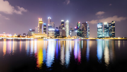 Obraz premium Illuminated modern city skyline reflecting on calm harbor at night.