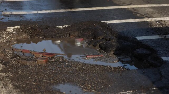 Urban scene with car passing by a big pothole in the asphalt