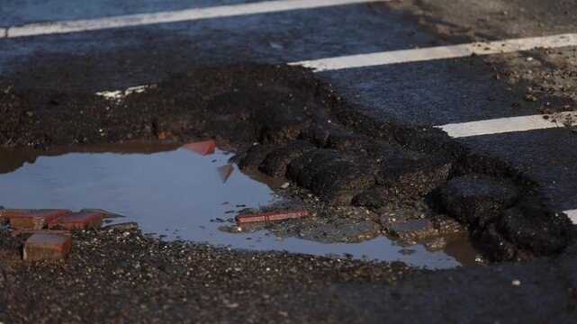 Urban scene with car passing by a big pothole in the asphalt