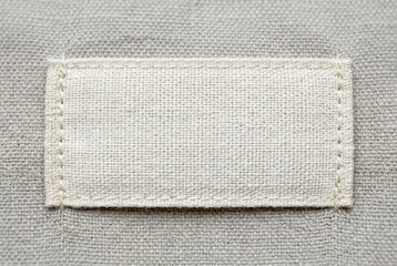 Fototapeta premium Blank white fabric label sewn onto gray textured material, realistic detail for clothing tags and branding options.