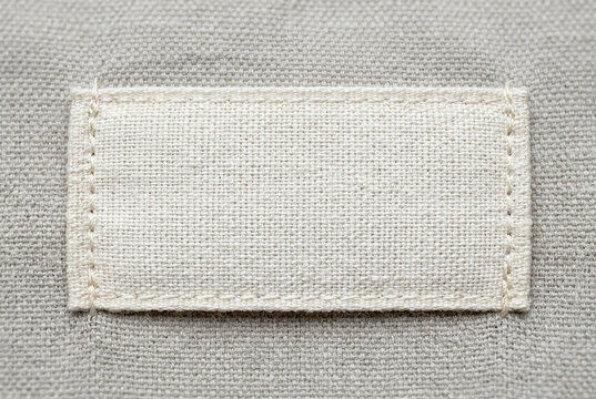 Blank white fabric label sewn onto gray textured material, realistic detail for clothing tags and branding options.