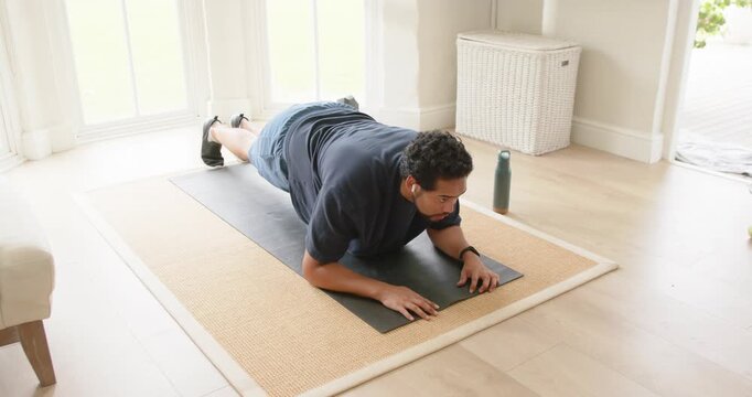 African American man in shorts placing forearms holding forearm plank at home on mat for strength