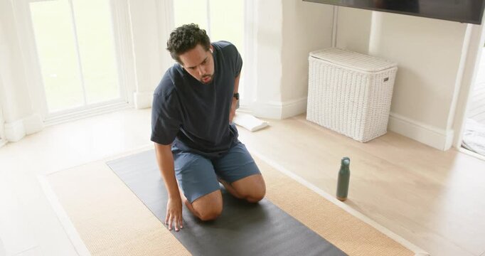 Man kneeling on black mat at home after glancing at screen, stretching back and steadying breath