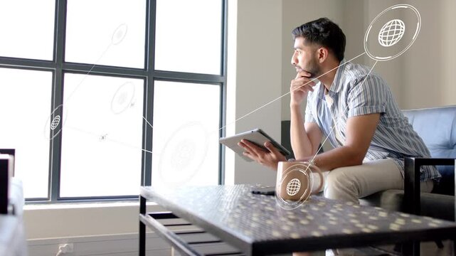 Man by window tapping tablet after network icons appearing, leaning into exploring technology