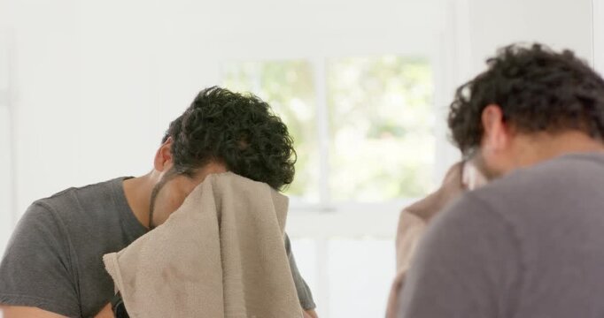 African American man bringing beige towel, drying face and neck, inspecting beard in mirror