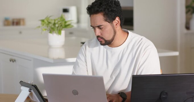 African American man in white tee working on silver laptop, viewing black monitor after alert
