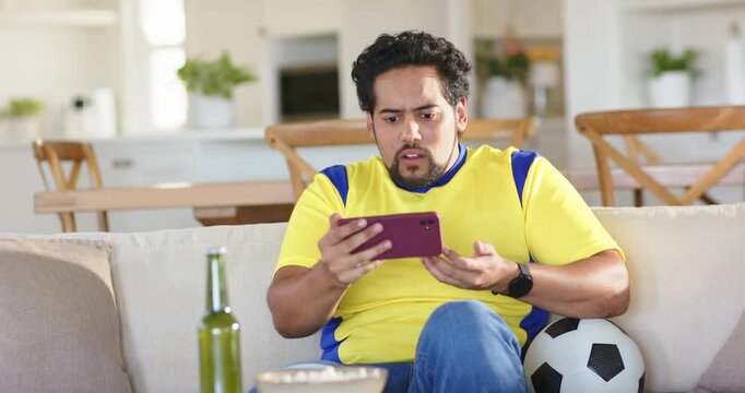 African American man on couch at home, holding purple phone, reacting to match, soccer ball nearby