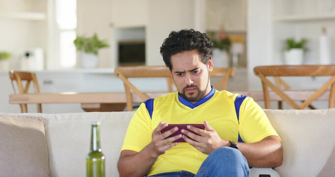 African American man sitting on couch tapping purple tablet, viewing, frowning, gasping, calming