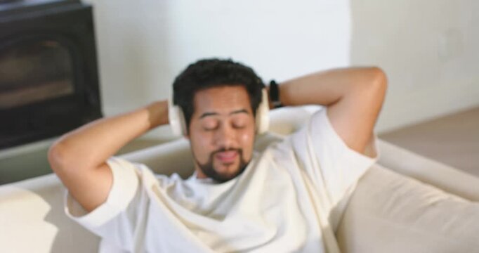 African American man putting on headphones, reclining on sofa in living room, closing eyes to relax